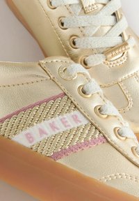 Kuldse tooniga tossud valgete ja kuldsete paeltega, roosa ja kuldse kudumisega küljetripud ning kummist tallad. Tossudel on "BAKER" bränding keelega ja külgedel.