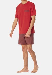 Camiseta de algodón roja con un bolsillo, combinada con pantalones cortos de patrón rojo y blanco. La prenda presenta mangas cortas y un corte relajado.