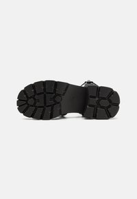 Semelle en caoutchouc noir avec des motifs de traction profonds et des rainures, dotée d'une surface texturée pour améliorer l'adhérence et la stabilité.