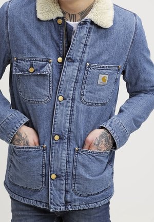 Jeansjacke in Blau mit cremefarbenem Kunstpelzkragen, mit zwei Brusttaschen und zwei unteren Taschen, die mit goldfarbenen Druckknöpfen verschlossen sind.