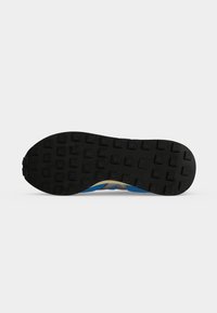 Semelle de chaussure en caoutchouc noir avec des motifs carrés sur la bande de roulement et un aperçu d'une tige bleue et beige sur fond blanc.