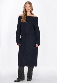Tengeri kék kötött kardigán ruha lecsúsztatott vállakkal, gombos elülső résszel, hosszú ujjakkal, derékövnél húzott kialakítással és bordás textúrával.