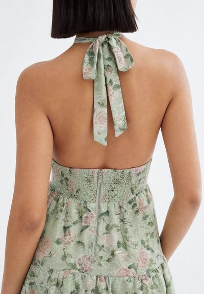 Woman wearing a sleeveless floral dress with a halter neck tie and a back zipper, showing bare shoulders and upper back.