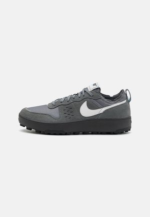 Chaussure de sport basse profil gris et noir avec dessus en suède et mesh, logo swoosh blanc, fermeture à lacets, et semelle robuste pour une bonne traction.