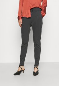 Mörkgrå taperade byxor med elastisk midja och dragsko, i kombination med en rostfärgad silkeskjorta och svarta pumps med spetsig tå.