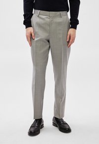 Calças cinza claro feitas sob medida com textura suave, corte justo e design frontal liso. Usadas com mocassins de couro pretos.