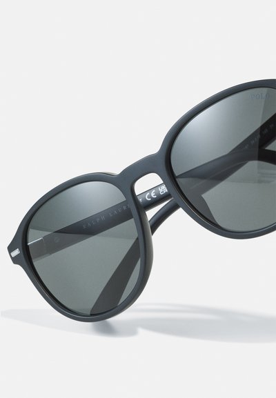 Melnas saulesbrilles ar matētu apdari, pārspīlēti apaļiem stikliem, tumši pelēkiem stikliem, ar gravējumu "RALPH LAUREN" uz kājas.