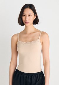 Beige singlet med tynne stropper og scalloped blondekant ved halsen. Mykt, tettsittende stoff kombinert med svarte shorts med snøring.