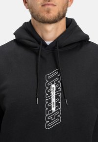 Felpa nera in cotone con logo bianco sul davanti. Il design include un cappuccio con coulisse e una vestibilità comoda.