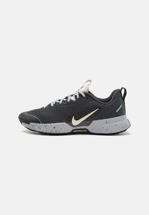 Czarno-szary but do biegania Nike Trail ATC z białym logo Swoosh, białymi sznurówkami, nakrapianą podeszwą i pętelką na pięcie.