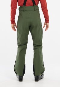 Pantalon de neige vert imperméable avec bretelles ajustables, conception fuselée, évents latéraux zippés et accents noirs au niveau des chevilles.