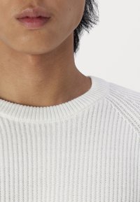 Maglione bianco a coste con scollatura arrotondata, che mette in mostra una fine texture e un design aderente. Senza motivi o accenti visibili.