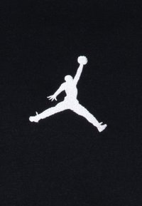 Svart tyg med en vit broderad Jumpman-logotyp, som visar en silhuett av en figur i en hoppande pose, som håller en basketboll.