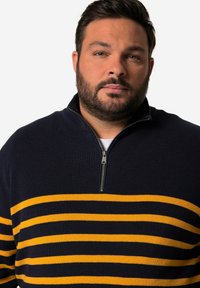 Námořnický svetr s žlutými vodorovnými pruhy, pletená textura a polo-zip límec. Má jednobarevný rám s pohodlným střihem.