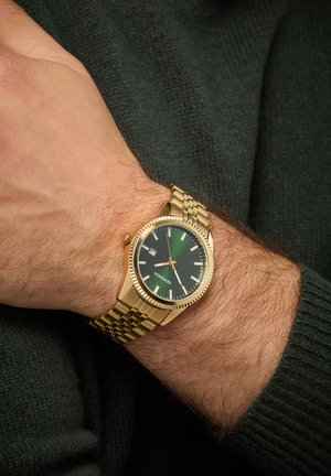 Goldfarbener Uhr mit grünem Zifferblatt, Metall-Mesh-Armbanduhr und erhabenen Markierungen. Verfügt über eine Datumsanzeige und eine strukturierte Lünette für zusätzliche Details.
