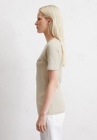 Camiseta de manga corta beige con un ajuste relajado, con escote redondeado y una textura sutil. Combinada con pantalones blancos para crear contraste.