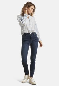Light blue shirt with floral embroidery, oversized sleeves, and ruffled cuffs. Paired with dark blue skinny jeans and white sneakers.