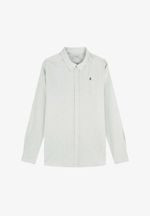 Cămașă lungă cu mânecă lungă, în dungi verzi deschise, cu guler cu buton și logo pe piept. Prezintă linii verticale subtile și butoane pe față.