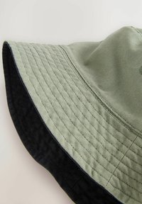 Groene katoenen bucket hat met een geribbelde textuur en een zwarte onderkant, voorzien van een brede rand en gestikte details langs de randen.