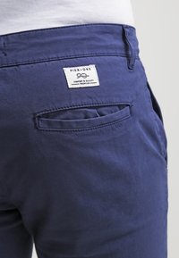 Navy blue cotton pants featuring a back pocket and a sewn label reading "PIER ONE" with "COMFORT & QUALITY PREMIUM" in white.