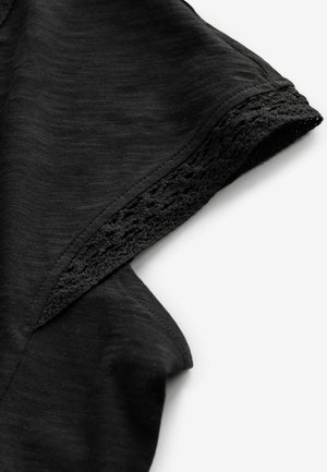 Schwarzer Stoff hat eine weiche Textur mit einem leichten Glanz, ergänzt durch einen gemusterten, gestrickten Rand entlang der Kante.