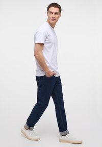 Cămașă albă cu mânecă scurtă, blugi albaștri din denim cu manșete răsucite și adidași albi cu accente de crem, purtate de un model masculin în picioare.