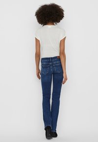 Vit kortärmad topp i kombination med mörkblå bootcut jeans, med subtil sömnad och en brun läderlapp på bakre midjan.