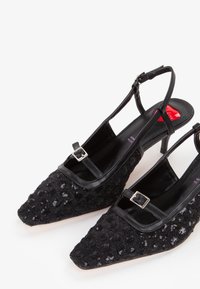 Scarpe slingback nere con punta affusolata, caratterizzate da una tomaia in paillettes testurizzate, dettaglio delò di fibbia piatta e un tacco alto e sottile.