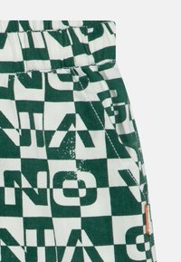 Tela a cuadros verde y blanco con patrones de texto en negrita. Incluye una cintura elástica y detalles de costura visibles.