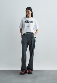 Valge T-särk musta "MOSCHINO" trükiga, hallid kõrge vöökohaga püksid ja burgundia tooniga jalanõud. Omaduseks on lõõgastunud istuvus ja soonikuga vöökoht.