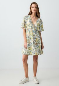 Abito a stampa floreale in tessuto leggero con scollatura a V profonda, maniche corte e vestibilità comoda, abbinato a sneakers bianche.