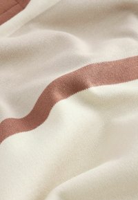 Bomuldsstof med en glat tekstur, der har et bølget design i crema og rustfarver, som fremhæver de kontrasterende farveinteraktioner.