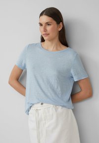 Lichtblauwe t-shirt met korte mouwen in een zachte, gestructureerde stof met een ronde halslijn, gecombineerd met witte broeken. Minimalistisch ontwerp, geen zichtbare patronen.