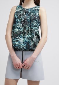 Top senza maniche con un motivo tropicale di foglie verdi e nere, design plissettato e tessuto morbido. Abbinato a una gonna grigia chiaro con zip.