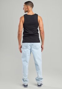 Mustaton hihaton toppi yhdistettynä vaaleansinisii löysiin farkkuihin ja mustiin kenkiin. Silkkinen kangas ja yksinkertainen muotoilu suoran leikkauksen kanssa.