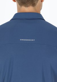 Blå kortærmet skjorte med et struktureret mønster, der har krave og "SWEDEMOUNT" logo i hvidt på ryggen. Glat stoffinish.