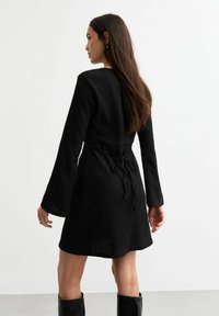Robe noire en jersey avec des manches longues, une taille cintrée à nouer et une jupe fluide. Tissu texturé et design minimaliste.