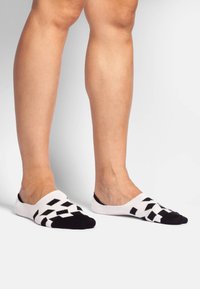 Schwarz-weiße Knöchelsocken weisen ein Diamantmuster auf der Fußsohle, eine glatte Stricktextur und ein niedriges Design auf, das die Zehen bedeckt.