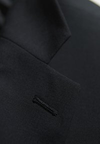 Schwarzer Stoff mit einer glatten Textur weist eine subtile Naht und ein kleines gesticktes Detail auf. Das Design umfasst eine klare, minimalistische Form.