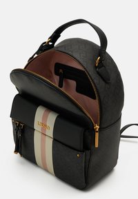 Sac à dos noir de créateur avec des rayures verticales beige et rose, fermetures éclair dorées, poignée supérieure et compartiment principal ouvert montrant des poches intérieures.