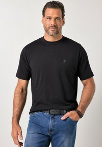 Zwart katoenen T-shirt met korte mouwen en een ronde hals, met een subtiel "JP"-logo in donkergrijs, gecombineerd met blauwe spijkerbroek.