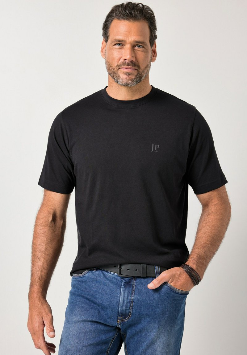 Zwart katoenen T-shirt met korte mouwen en een ronde hals, met een subtiel "JP"-logo in donkergrijs, gecombineerd met blauwe spijkerbroek.