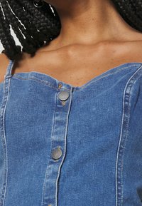 Denim top featuring a V-shaped neckline, thin straps, and metal buttons down the front. The fabric is blue with a slightly textured finish.