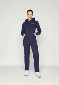 Mørkeblå hettegenser med lomme foran, snøring i hetten og logo på brystet, kombinert med matchende tettsittende bukser. Stoffet ser jevnt og mykt ut.