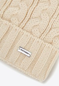 Kremowa dzianinowa czapka z wzorem warkocza i prążkowaną fakturą, z przymocowaną srebrną metką z napisem "WITTCHEN".