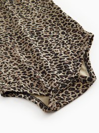 Bodysuit en imprimé léopard en tissu doux, avec une base beige, des taches marron foncé et des accents noirs. Comprend une fermeture à pression à la base.