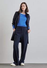 Tvådelad outfit bestående av en blå topp och mörknavy vida byxor, kombinerat med vita sneakers. Tyget verkar mjukt och skräddarsytt.