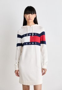 Abito felpa color crema con strisce orizzontali blu navy e rosse, caratterizzato dal logo "TOMMY JEANS", polsini a coste e cappuccio regolabile con cordino.