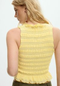 Kollane smock-top rippidega dekoltee ja mustade triipudega. Kerge kangas, kitsejoonega siluett laieneva hemina ja õhukeste rihmadega.