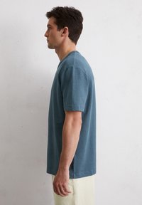 Teal katoenen T-shirt met korte mouwen en een ronde hals, met een rechte snit en zijsplitten, gedragen met lichtgekleurde broeken.